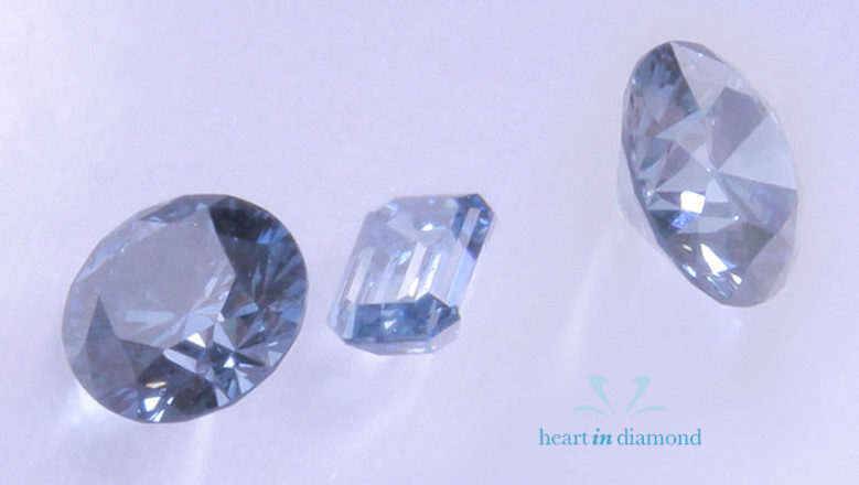 Three fancy blue cremation diamonds. Two round cut and 1 emerald cut with heart in diamond logo