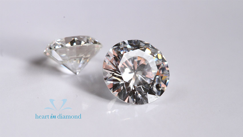 2 white round cut diamonds shown from 2 different angles with the heart in diamond logo